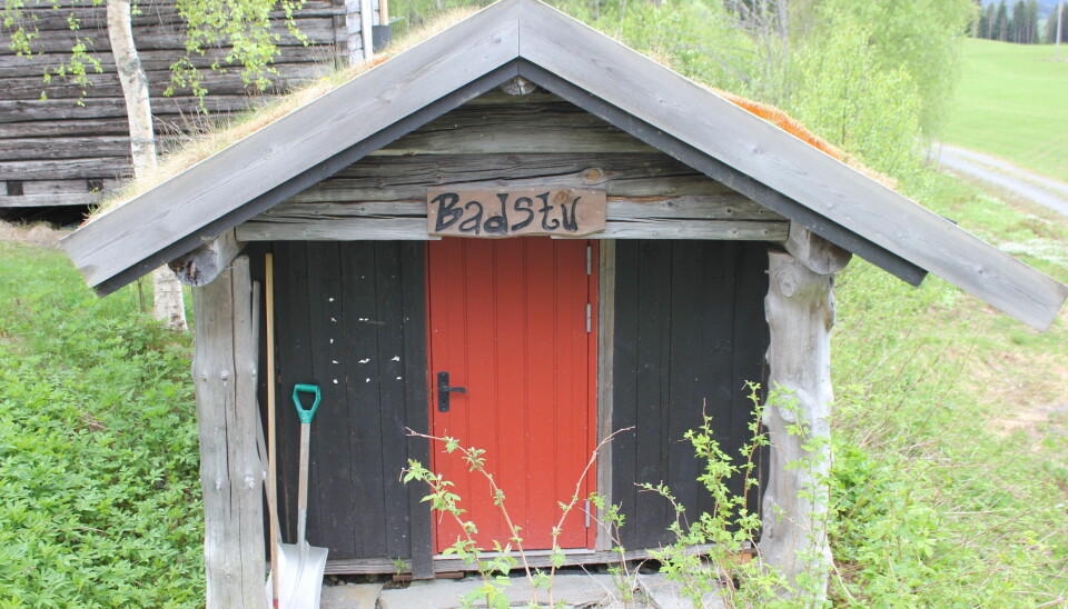 Et lite sort hus med rød dør over er et skilt hvor det står 'badstu'
