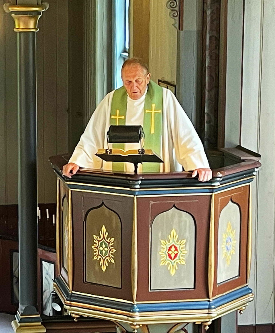 En prest i hvit skjortel med grønt rundt halsen og kors holder preken