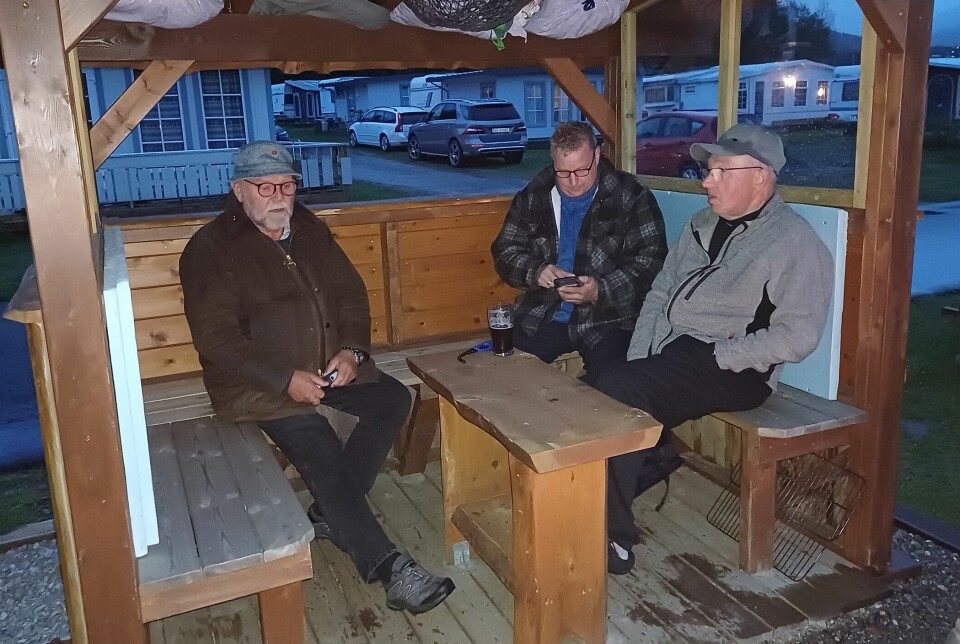 Tre fiskere sitter på benker i en liten gapahuk