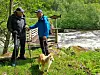 To menn og en hund ved ei lita gangbru over ei elv.