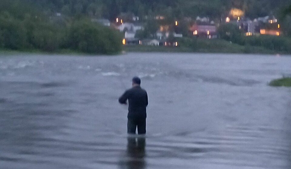 En mann som står ute i elva og fisker.