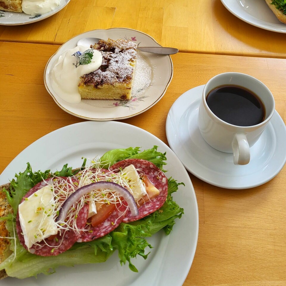 En baguett, eplekake med krem og en koppkaffe på et pådekt bord.