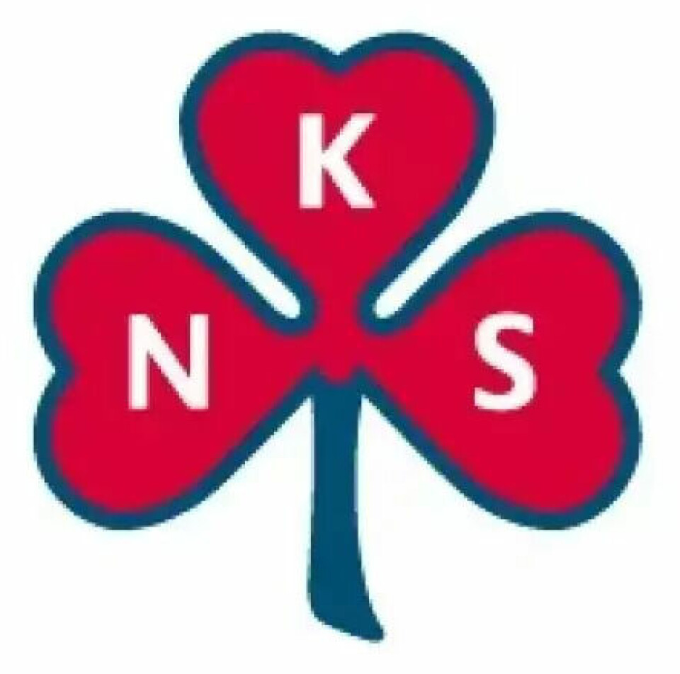 Sanitetsforeningens logo. En rød trekløver med blå kant rundt. En bokstav på hvert blad: N, K og S.