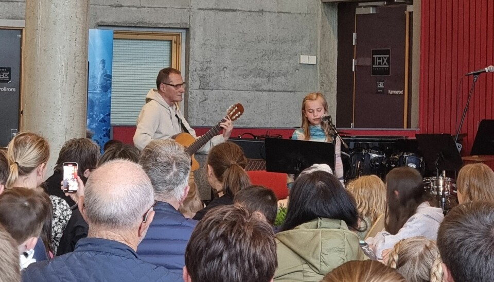 Publikum følger med på en liten jente som synger i mikrofon og en mann som spiller gitar.