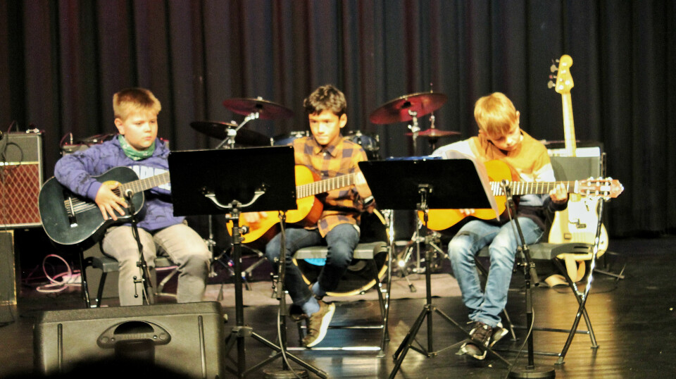 Tre gutter sitter på scenen og spiller gitar.