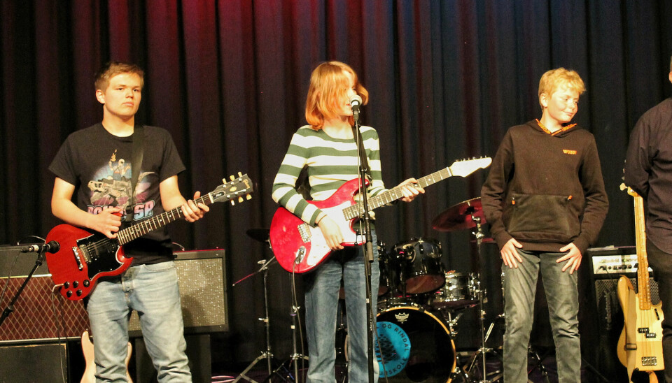 Tre ungdommer står på scenen. To holder gitarer.