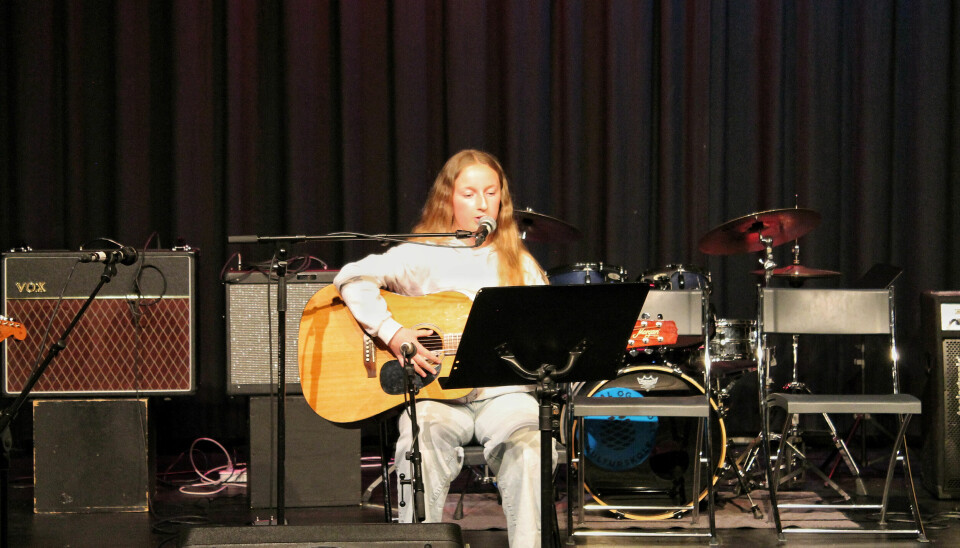 En jente sitter på scenen. Hun spiller gitar.