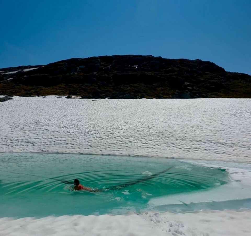 En kvinne isbader i en dam hvor isen har smeltet på fjellet, det er fortsatt mye snø rundt vannet