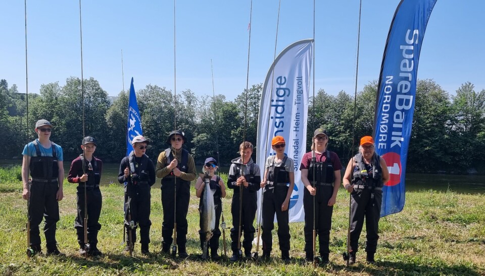 8 barn og 1 voksen står med fiskeutstyr og smiler mot kamera