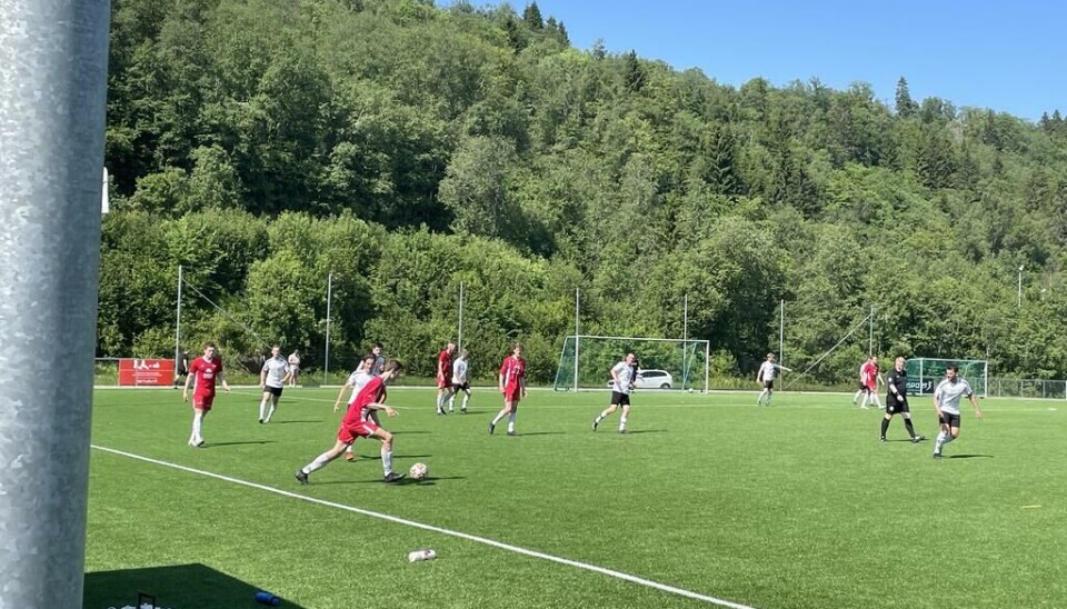 Svorkmo - Rindal Et fotballag i røde drakter spiller mot et lag med hvite drakter på en gressbane med trær i bakgrunnen.