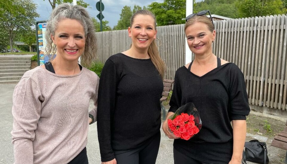 Tre smilende damer ute foran et gjerde med trær i bakgrunnen.