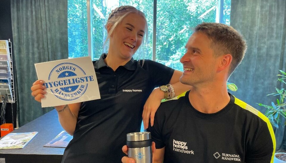 Tony Sæterbø har fått seg klistremerke og kopp hvor det står 'NORGES HYGGELIGSTE HÅNDVERKER' etter Mari Ranes Eidsli nominerte han til konkurransen. Damen holder et klistremerke og mannen en kopp. De kikker på hverandre og smiler/ler.