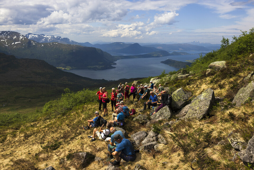 Ei gruppe på nærmere 30 turkledde pensjonister som har tatt en rast i ei fjellside. Fjord og fjell i bakgrunnen.