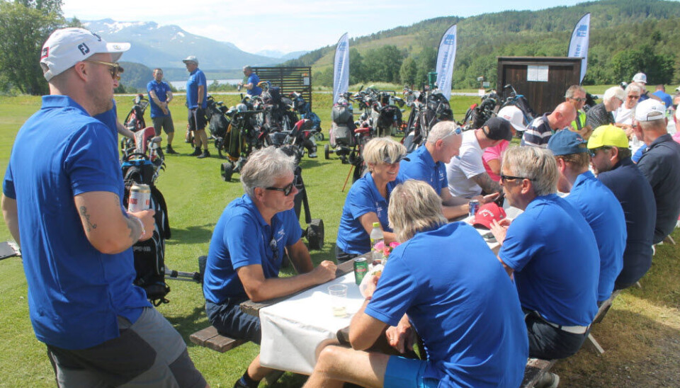 Mange mennesker sitter på benker på en golfbane og spiser mat