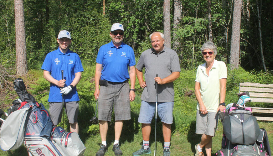 3 menn og 1 kvinne står med golfbaggene sine og smiler mot kameraet
