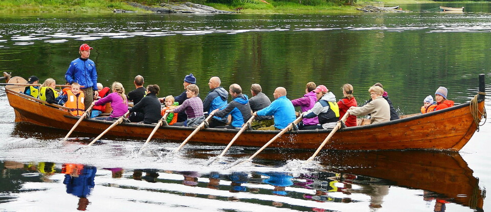 Mange mennesker i en lang robåt ror på fjorden
