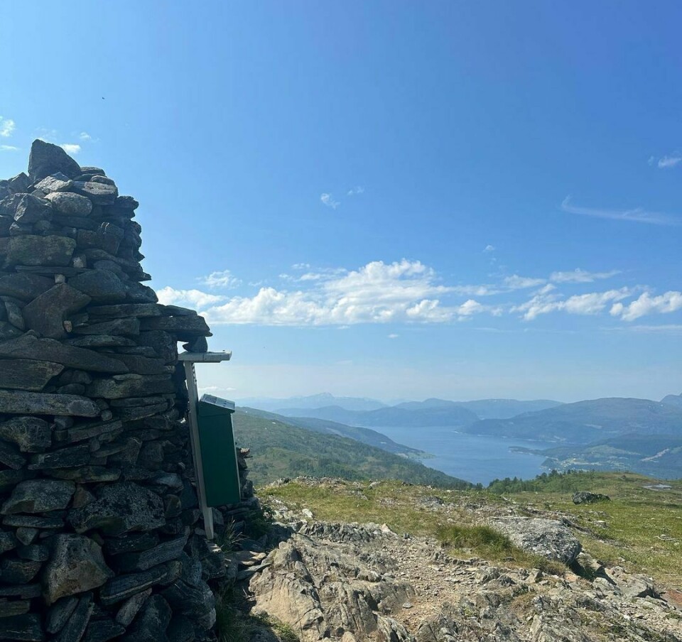 En varde på toppen av et fjell med utsikt over fjorden og blå himmel