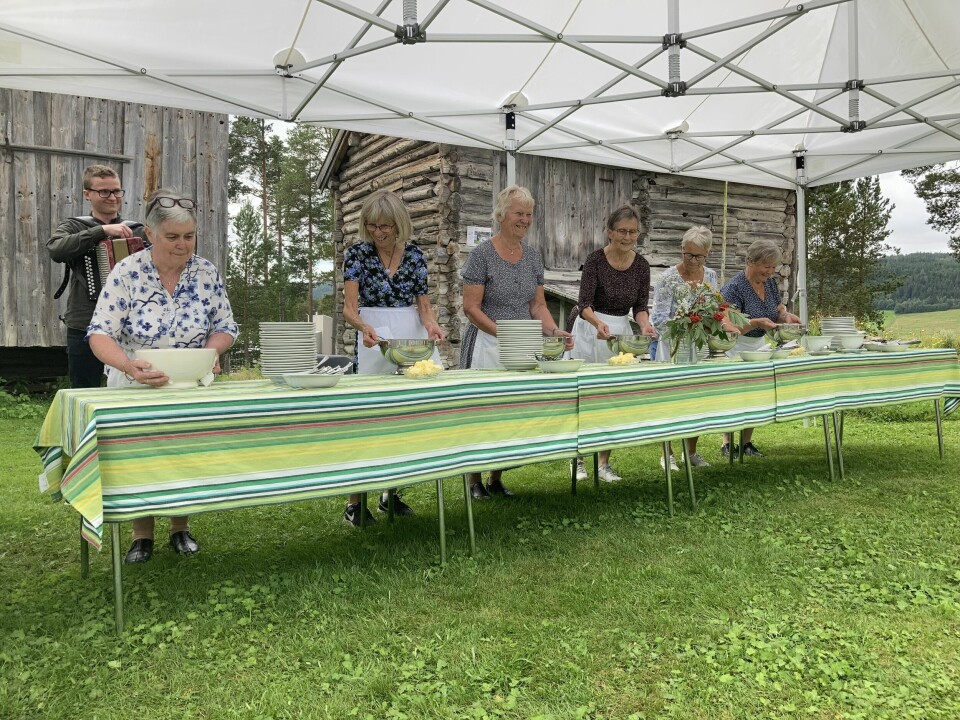 Eldre kvinner står bak et langbord på gresset og serverer grøt