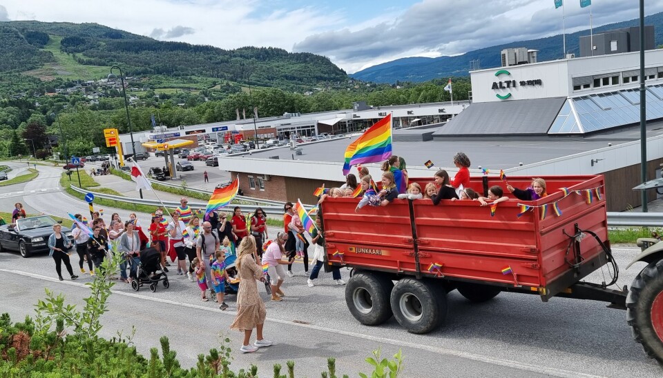 Mennesker står i en henger på en traktor og går bak den i et tog med regnbueflagg