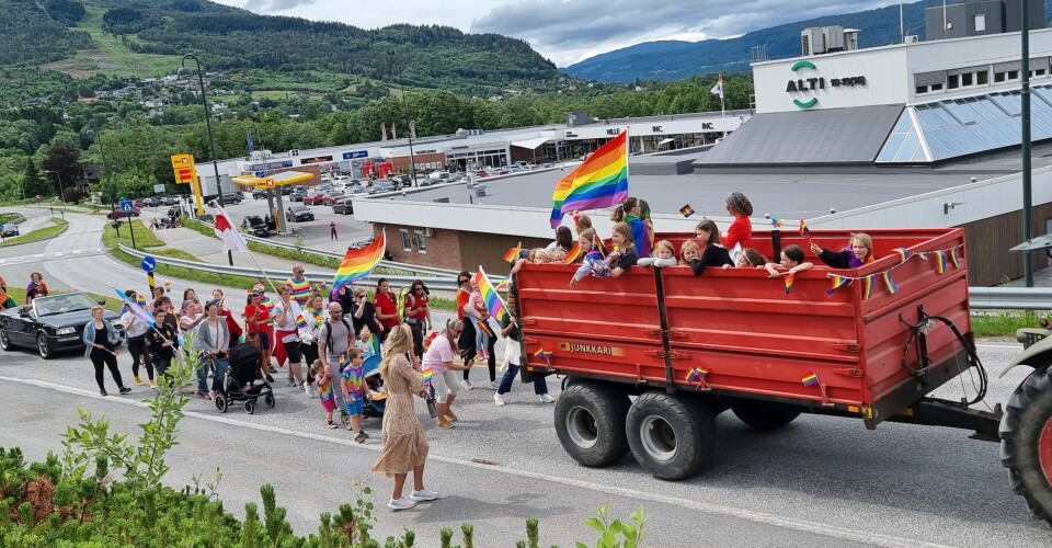 Mennesker står i en henger på en traktor og går bak den i et tog med regnbueflagg