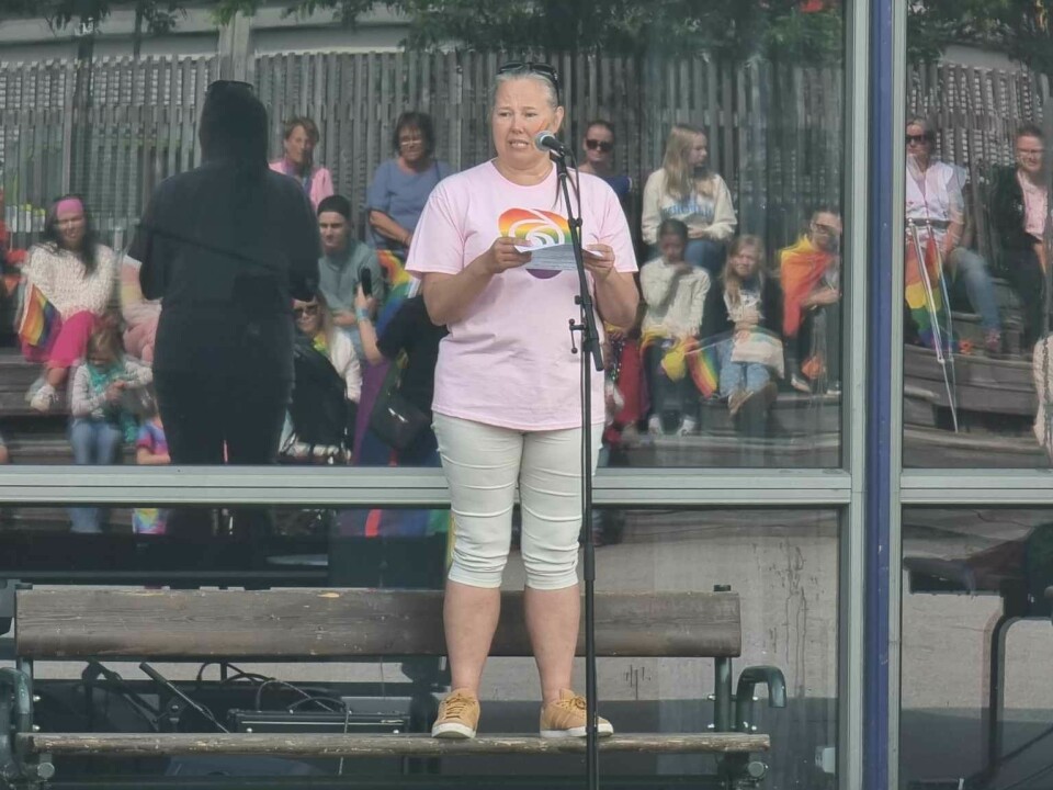 En kvinne kledd i rosa står på en benk og taler i en mikrofon