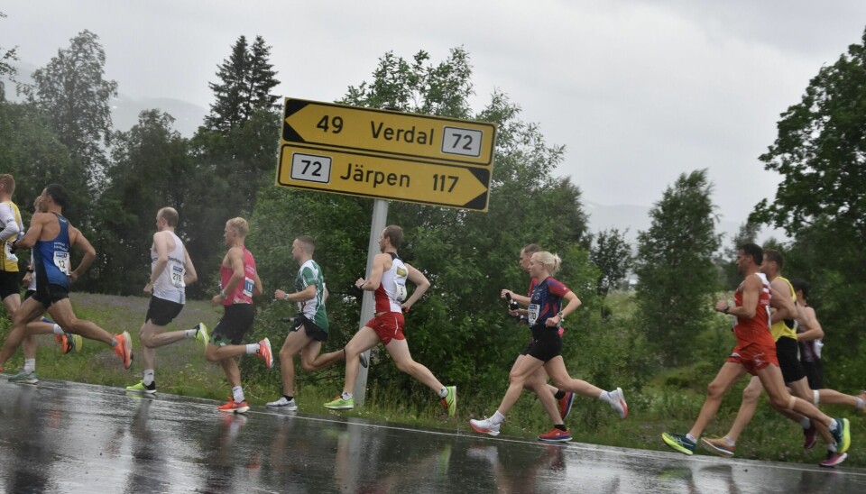 Menn og kvinner i treningsklær løper langs vegen i regnvær