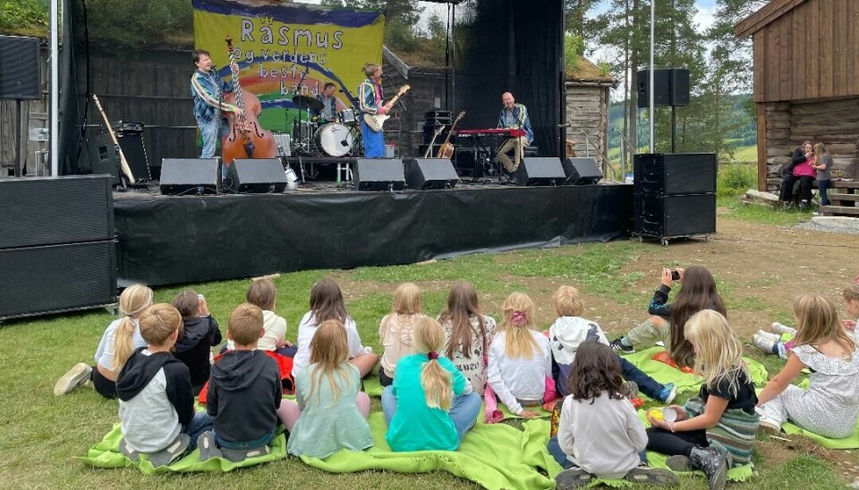 Fire musikere på en scene. Sittende barn foran scena.