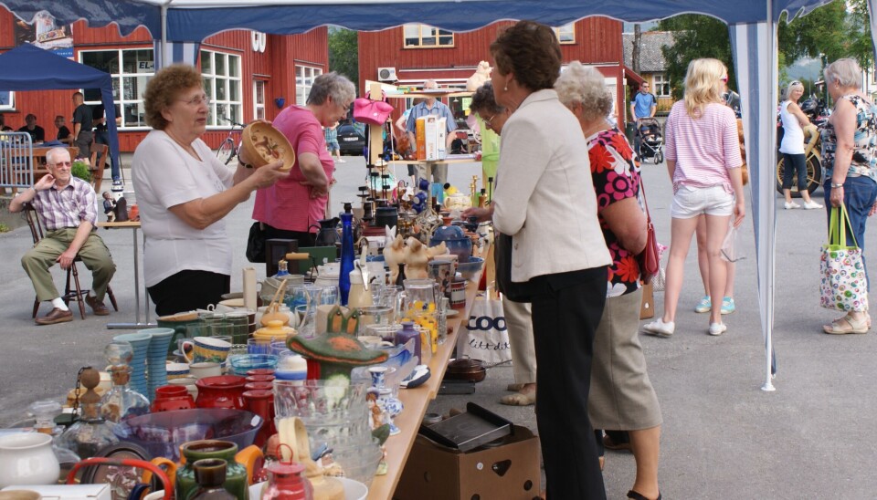 Et bord med lopper (lloppemarked) på en asfaltert plass, og noen damer som selger og noen som kjøper.