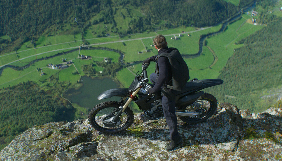 En mann står med en motorsykkel på toppen av et fjell og ser ned mot bakken