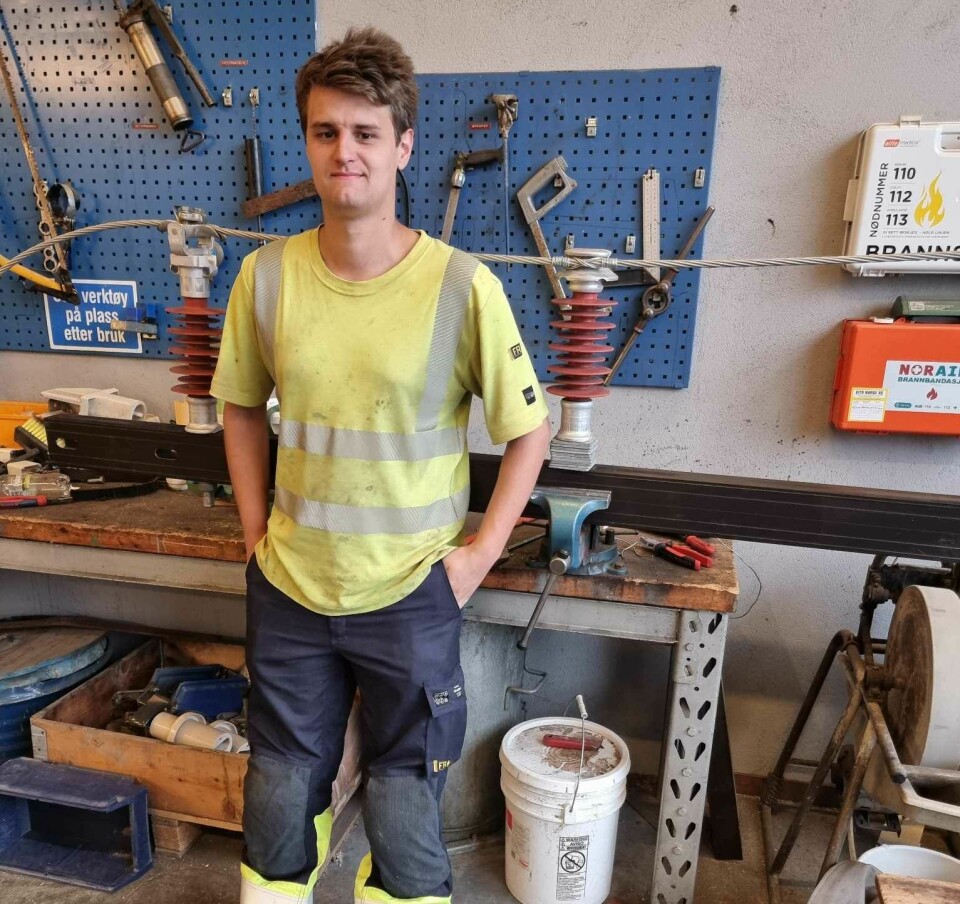 En ung mann står kledd i arbeidsklær foran diverse verktøy.
