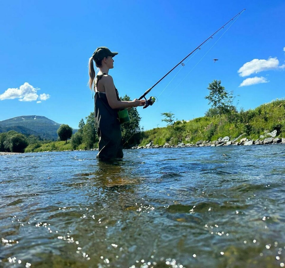 En ung dame står i elva og fisker laks