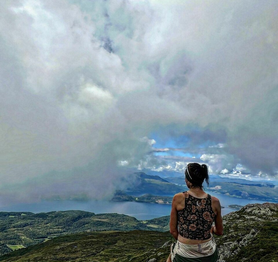 En kvinne sitter med ryggen til kameraet på toppen av et fjell og ser nyter utsikten