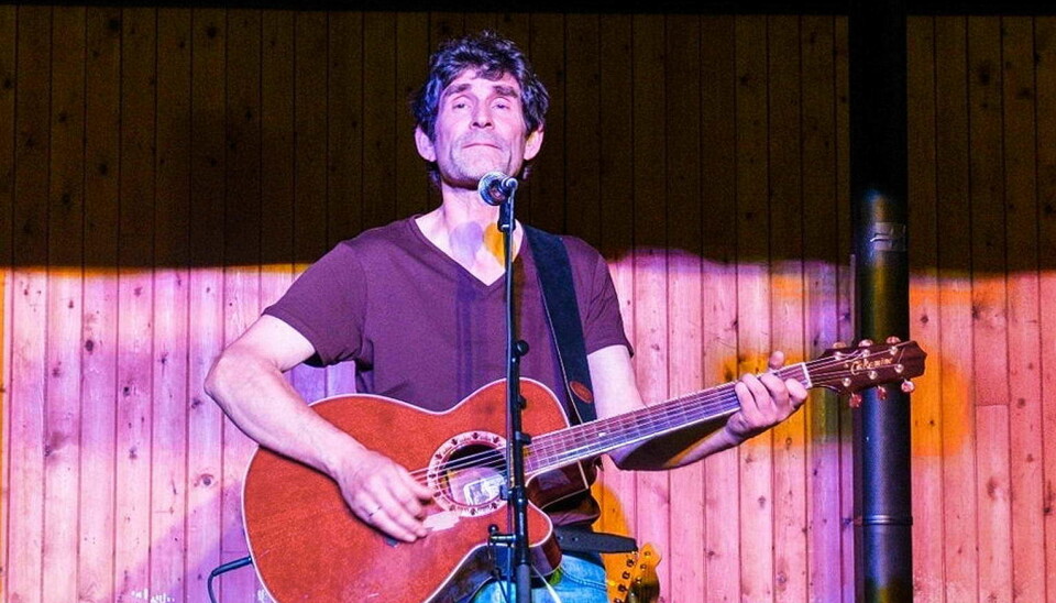 En mann synger i en mikrofon og spiller gitar