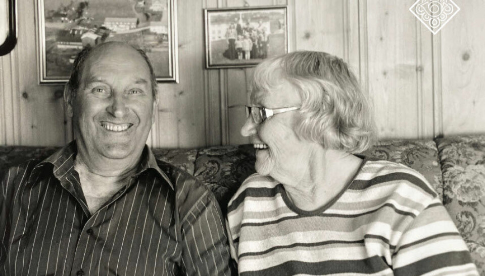 Et sort hvitt bilde av en mann og en dame som sitter i en sofa og ler.