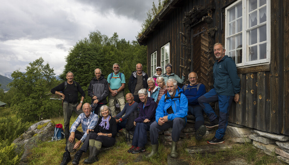 En gjeng pensjonister kledd i turklær sitter foran veggen på en hytte