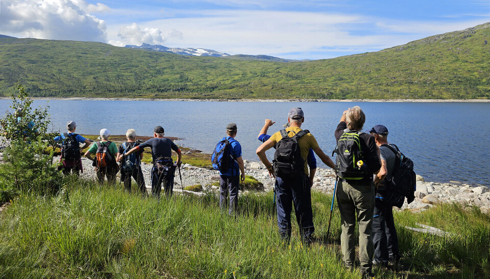 Pensjonister står ved sjøkanten og ser over på fjellene på andre siden