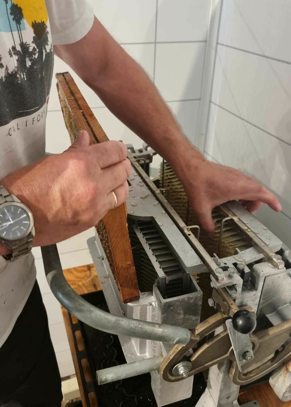 En mann bruker en maskin som presser honningen lettere ut av tavlene