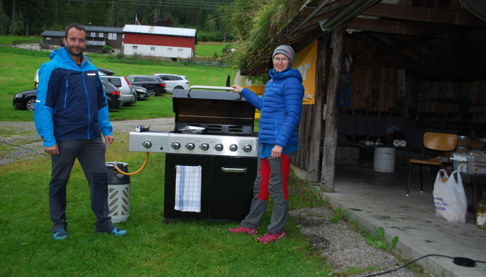 En mann og en dame står ved en gassgrill på en gressplen