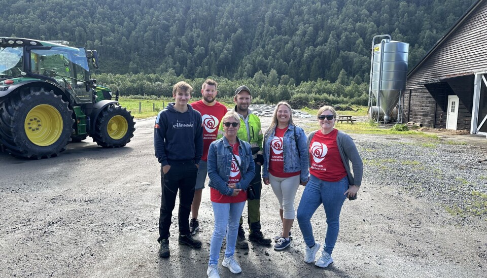 En bonde og en dreng står med 3 kvinner og en mann i røde t-skjorter med Arbeiderpartiet sin rose som logo. De står på en gårdsplass foran en grønn og gul traktor.