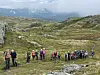 Ca 25 mennesker på et fjell. Går/står etter hverandre på en sti.