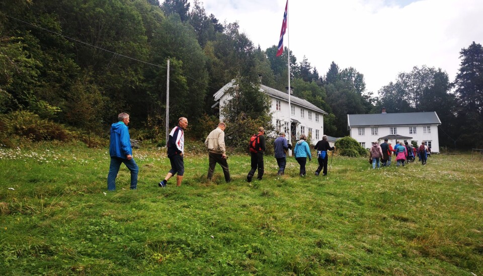 Trøinn. Årnesdagen. Fere personer som går i rekke inn på et gammelt gårdstun, der flagget er heist.