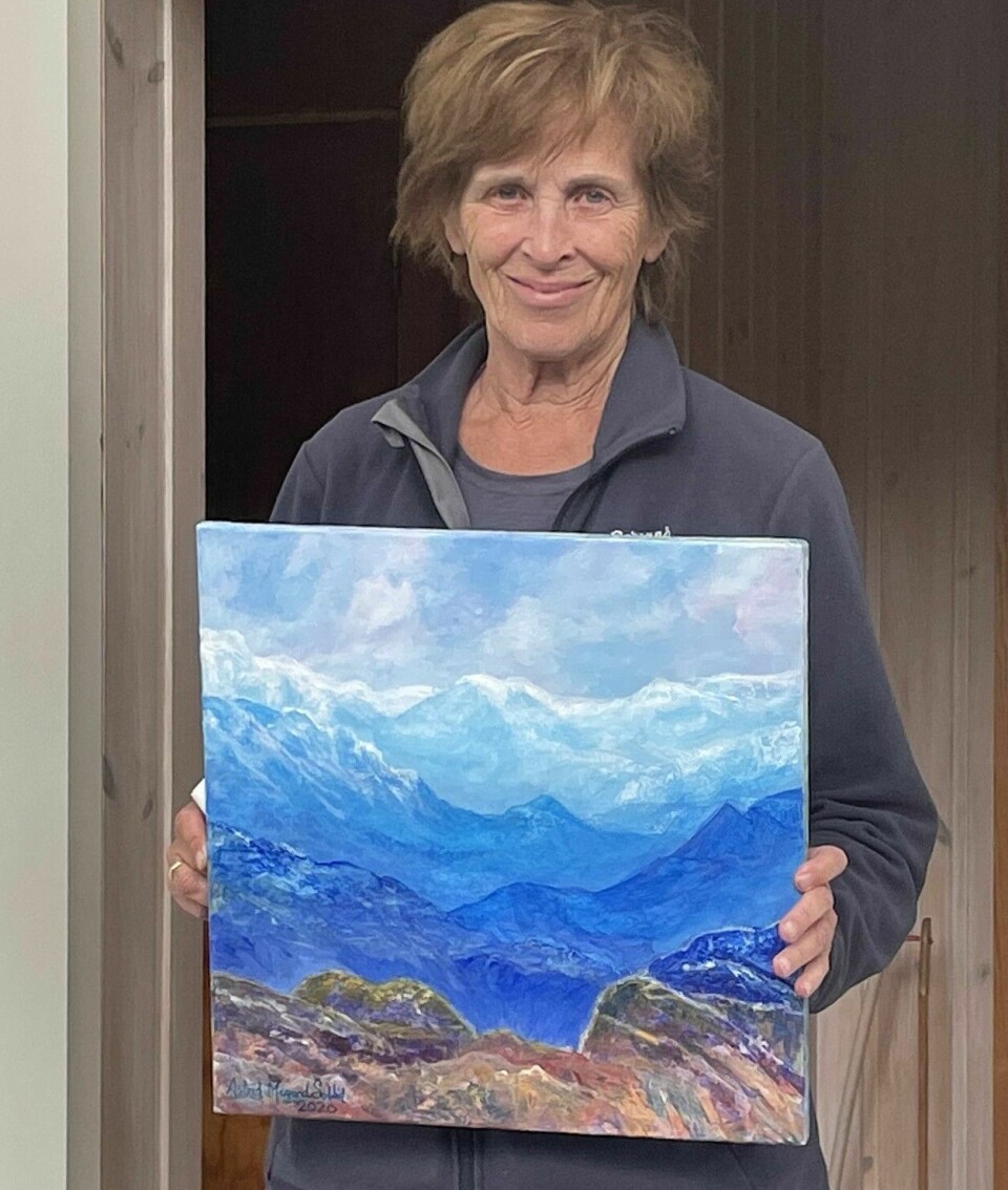 Dame held eit maleri av fjell og himmel.