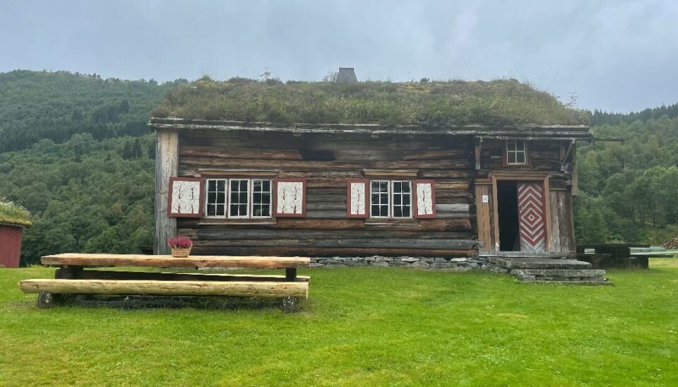 Tømmerhus. Bord og benker foran med blomster på bordet.