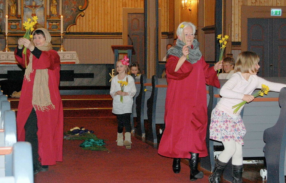 Noen barn og voksne med påskeliljer inne i ei kirke.