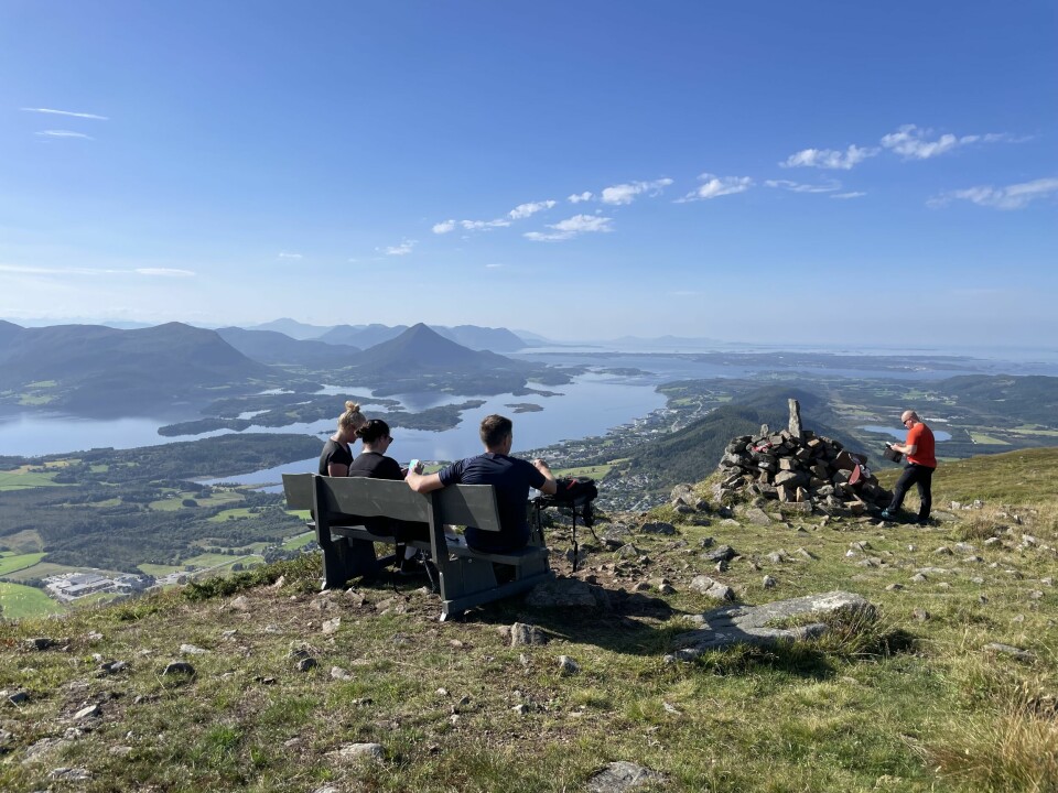 Tre mennesker på en benk på en fjelltopp. Fjord og fjell i bakgrunnen.
