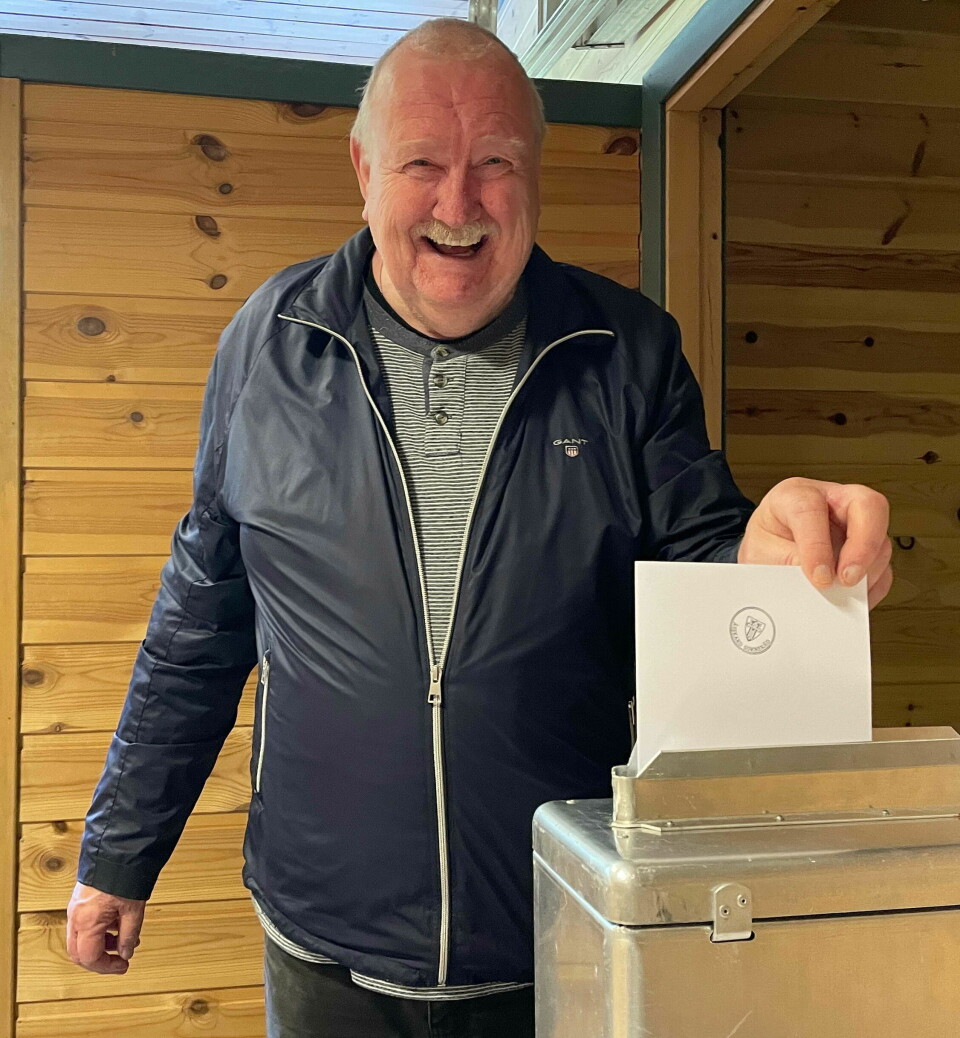 En smilende mann som putter sin stemme opp i valgurnen.