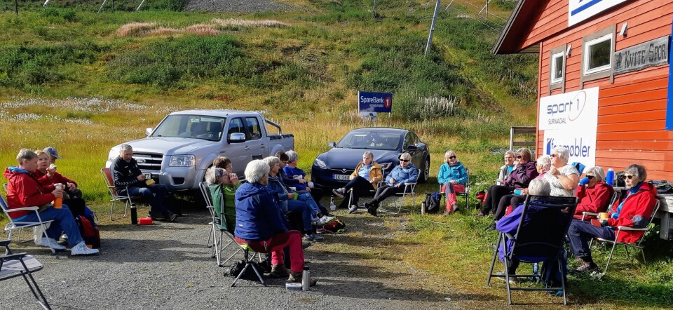 Ei gruppe turkledde pensjonistar som tar ein matpause på ein parkeringsplass.
