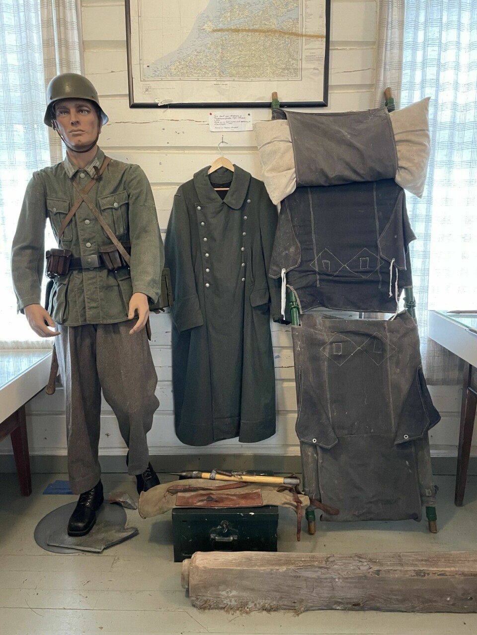 Dukke med krigsklær og -utstyr, frakk på en kleshenger og en båre