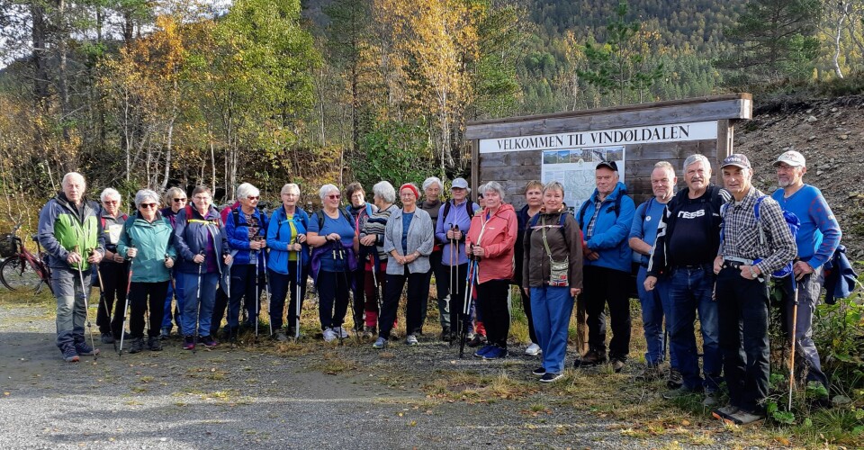 Ei gruppe turkledde pensjonister oppstilt ved et skilt der det står 'Velkommen til Vindøldalen'.
