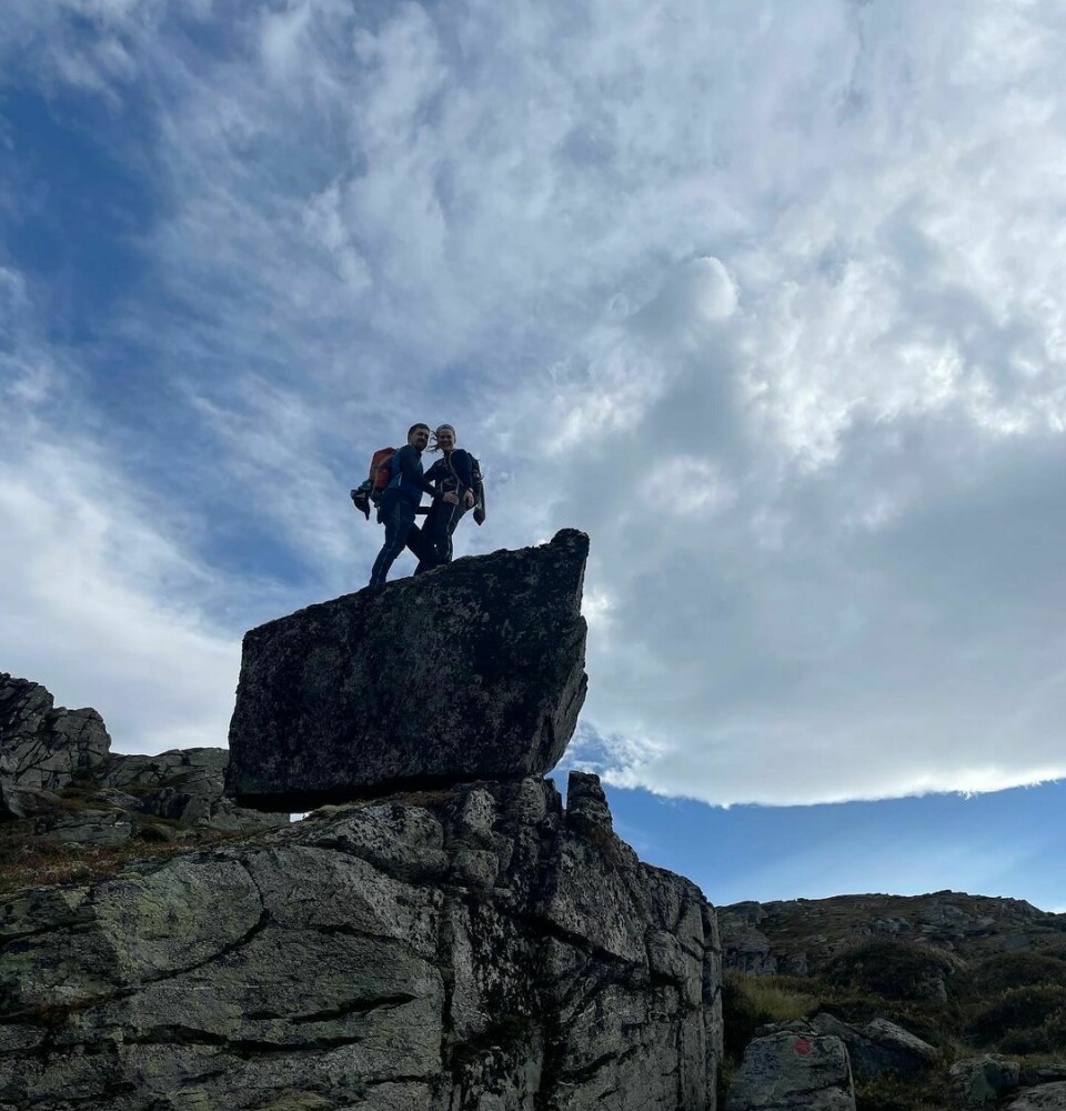 To mennesker står på en stor sten som ligge og balanserer på en fjellvegg